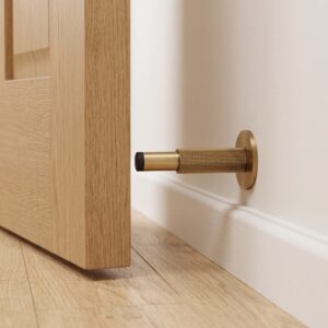 Aged brass knurled wall mounted door stop with rubber bumper beside an open wooden door