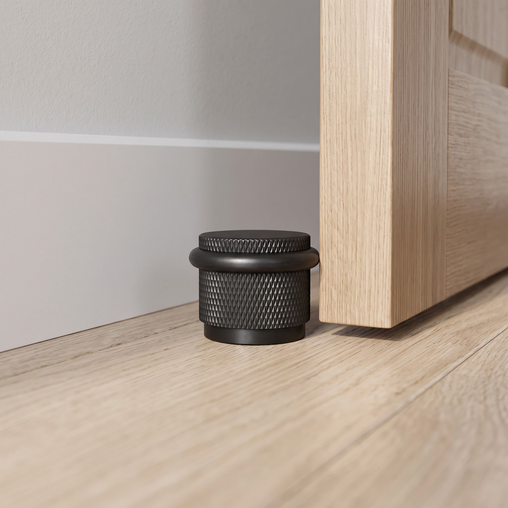 Black brass knurled floor mounted door stop with rubber bumper beside a wooden door