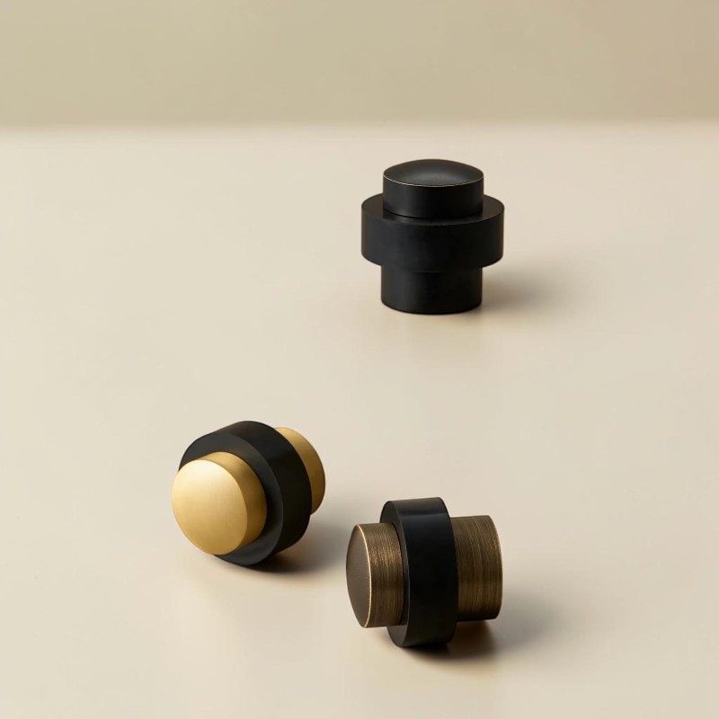 Three cylindrical floor door stops in Black Brass, Brushed Brass and Aged Brass