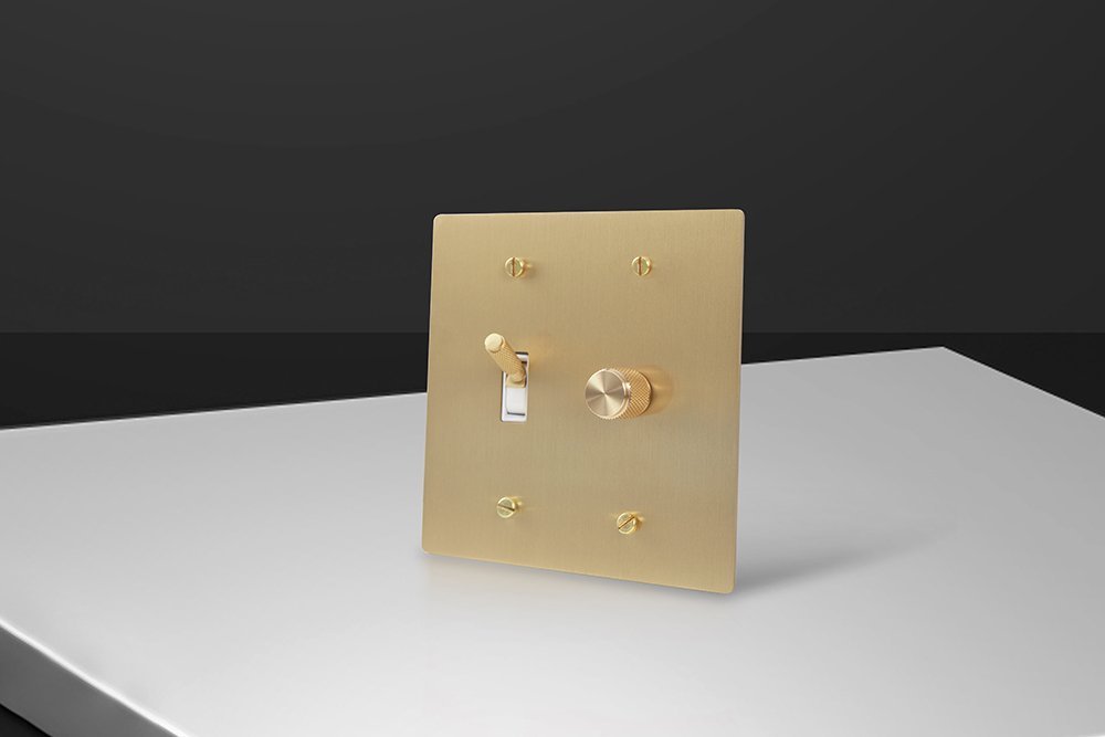 Brass toggle with a white surround and brass rotary lighting dimmer, photographed at an angle.